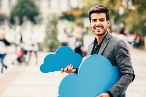 Ein junger Mann hält zwei blaue Wolken in den Händen und lächelt zufrieden in die Kamera.