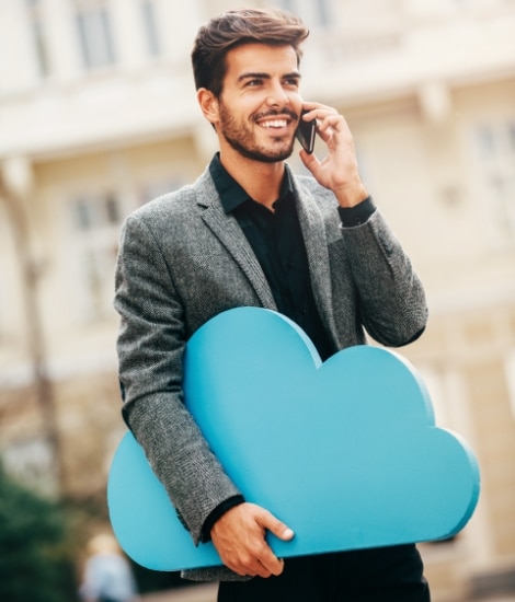Ein junger Geschäftsmann steht auf der Straße und telefoniert mit seinem Smartphone - dabei hält er eine Cloud in der anderen Hand.