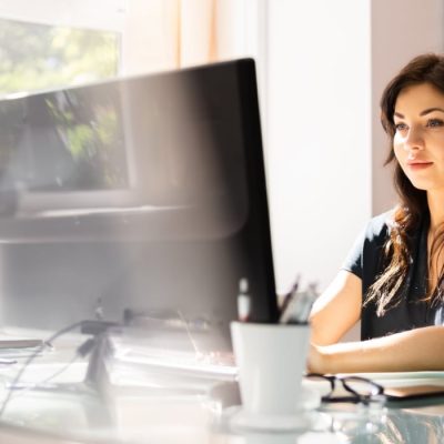Eine junge Geschäftsfrau sitzt an Ihrem Computer und arbeitet konzentriert. Sie sieht zufrieden aus, daher Sie sich auf Ihr IT-Netzwerk verlassen kann.