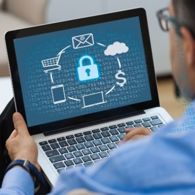Ein Mann sitzt auf einem Stuhl - er hält einen Laptop. Auf dem Bildschirm ist eine IT-Sicherheitssoftware zu sehen, die seine Daten schützt.